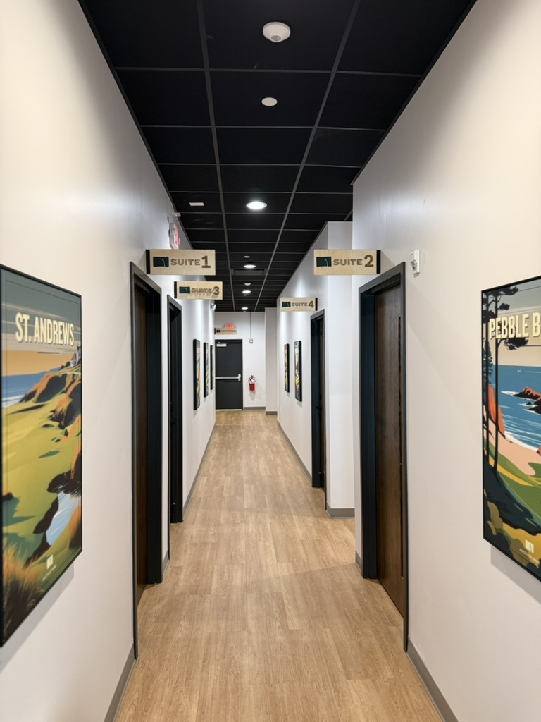 A private suite hallway lined with numbered Sim Suite doors and framed course art