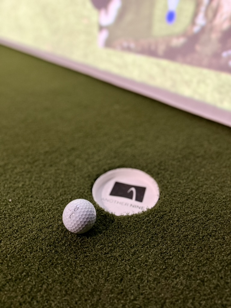 Golf ball beside an Another Nine tee marker on the turf